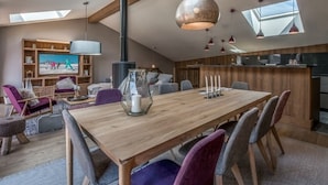 A modern loft with a high ceiling, skylights, a central fireplace, a dining area with a wooden table, and a cozy seating arrangement.
