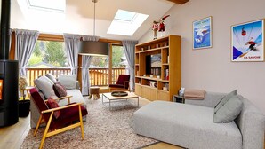 A cozy living room with a fireplace, a sofa, a red chair, a bookshelf, and a large window with curtains.