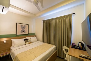 A hotel room with a bed, a desk, a chair, a television, and a window with curtains. - Olive Hotel JP Nagar by Embassy Group (Bengaluru)