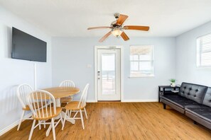 Ein Essbereich mit Holztisch und -stühlen, einem Deckenventilator, einem schwarzen Ledersofa und einem an der Wand befestigten Fernseher.