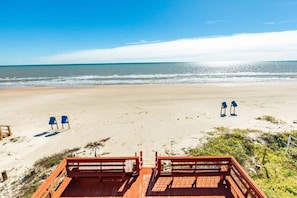 Ein Strand mit einer Holzterrasse, zwei blauen Stühlen und einem Geländer.