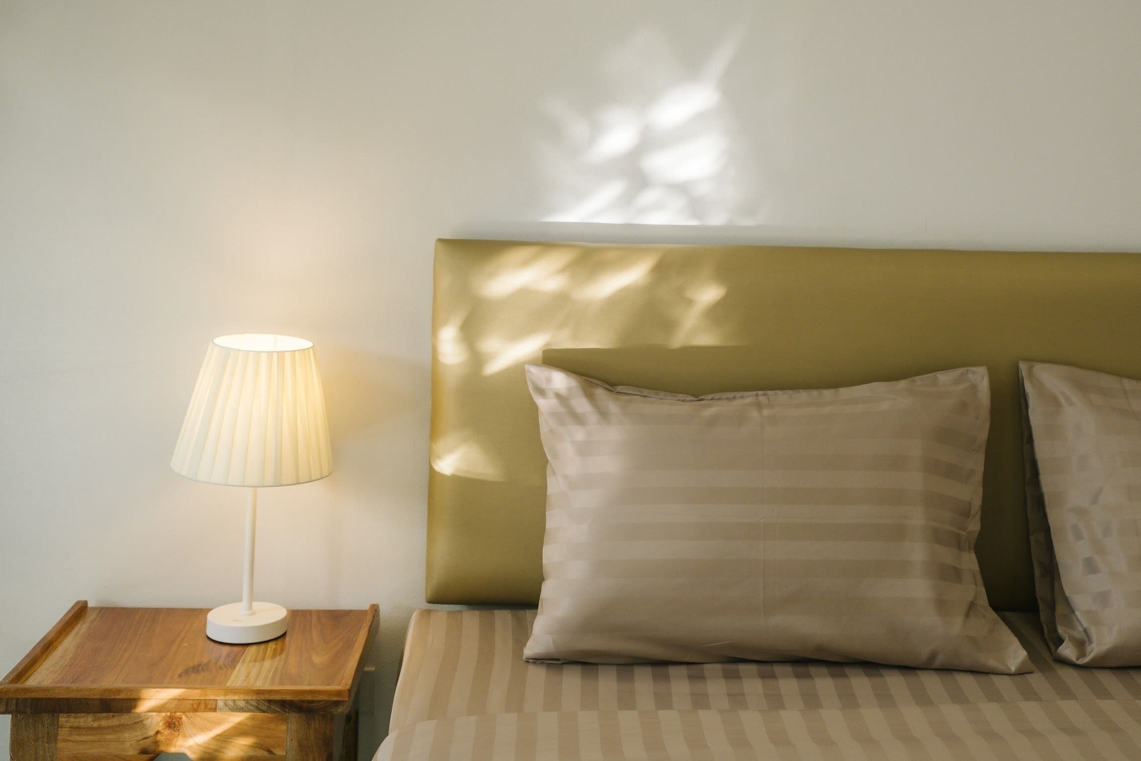 A neatly made bed with striped bedding, a bedside lamp, and a headboard with a leaf pattern.