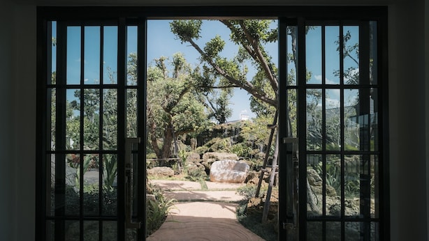 Vista a través de un portón de madera que da a un jardín con un sendero, rocas y árboles.