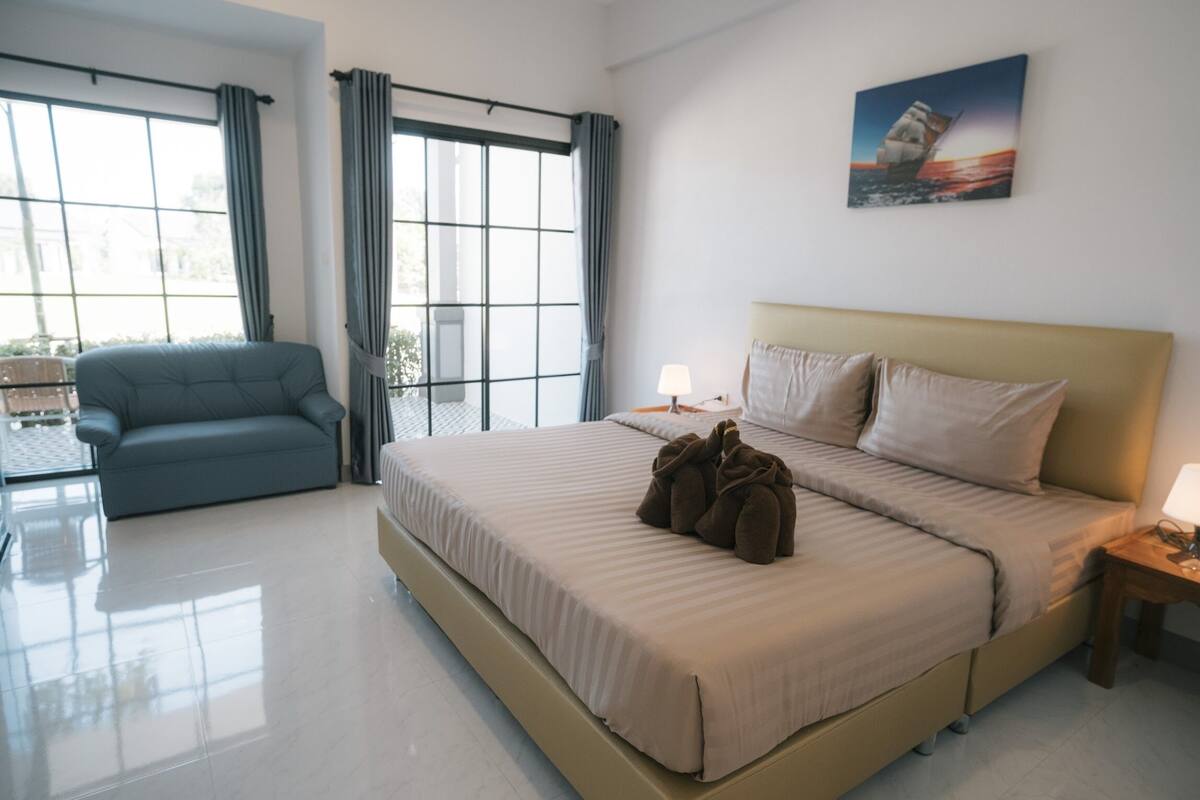 A modern hotel room with a large bed, a sofa, a window with curtains, and a painting on the wall.