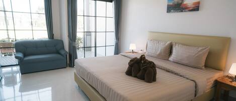 A modern hotel room with a large bed, a sofa, a window with curtains, and a painting on the wall.