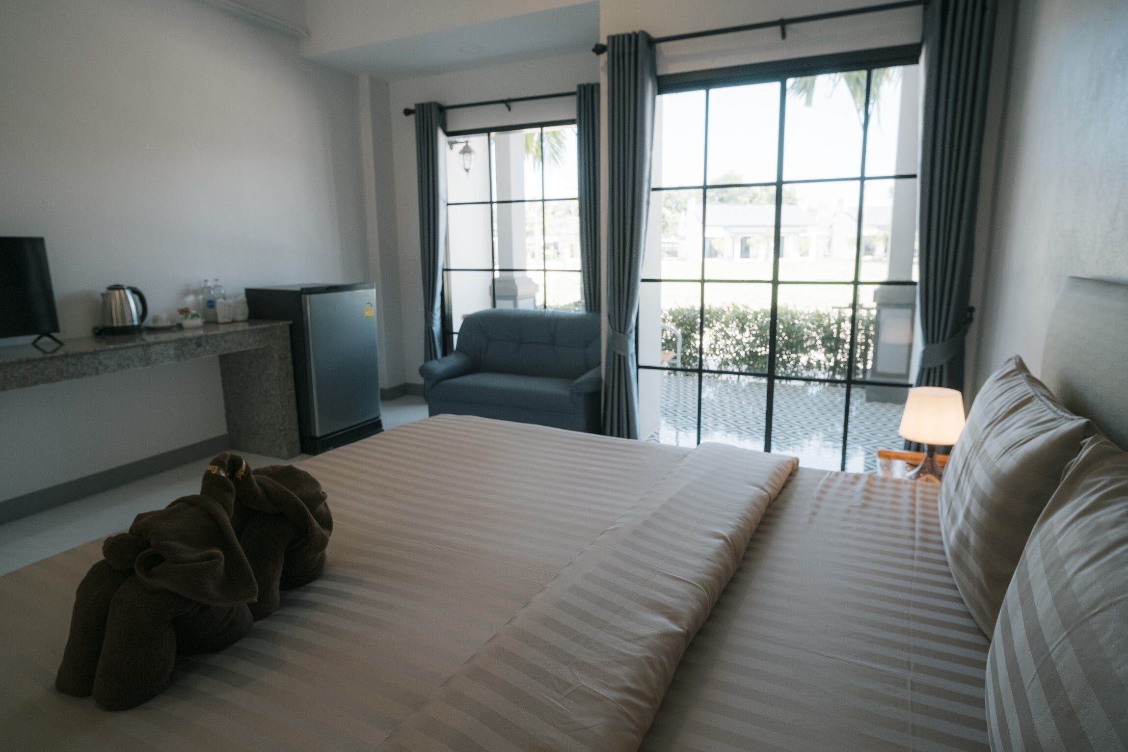 A hotel room with a bed, a desk with a computer, a chair, and a window with curtains.