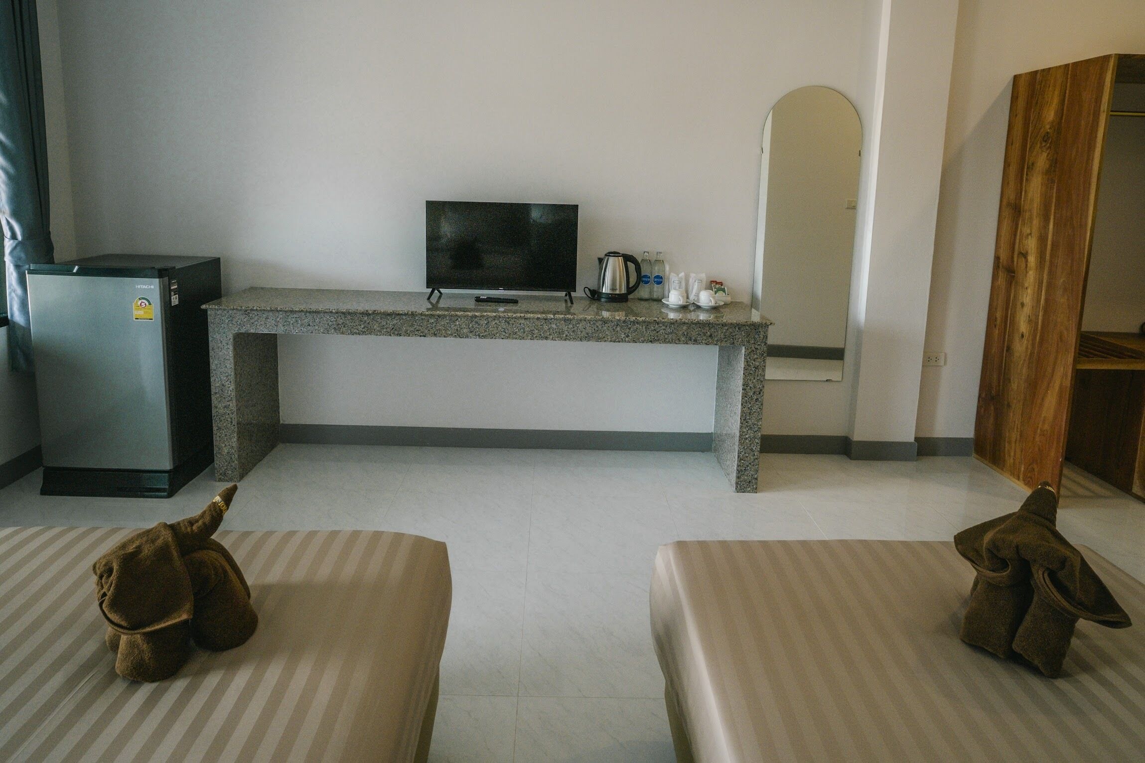 A hotel room with a television on a granite console, a small refrigerator, a coffee maker, and two cushioned seating areas.