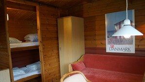 Une pièce de cabane en bois avec des lits superposés, un canapé rouge, une armoire en bois et une affiche représentant une scène de plage.