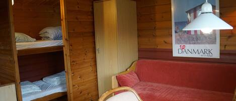 Een houten kamer met stapelbedden, een rode bank, een houten garderobe en een poster van een strandgezicht.