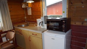Une cuisine compacte avec des meubles de rangement en bois, un évier, un four à micro-ondes et un petit réfrigérateur.