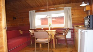 L’intérieur d’un chalet accueillant, avec un plancher en bois, un canapé rouge, une table à manger avec des chaises, un coin cuisine et une fenêtre avec des rideaux.