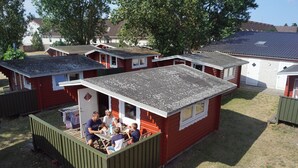 Une petite maison mobile rouge, dotée d’une véranda où un groupe de personnes est assis autour d’une table.
