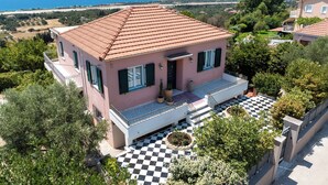 Una villa rosa con techo de tejas, un patio a cuadros y vistas al mar.