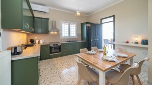 Una cocina moderna con armarios verdes, una mesa de comedor de madera y un amplio ventanal.