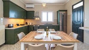 Una cocina moderna con gabinetes verdes, una mesa de comedor de madera para cuatro personas y un amplio ventanal que proporciona luz natural.
