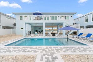 Un edificio de dos pisos con piscina, mobiliario exterior y un patio cubierto.