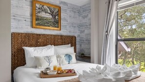 En pænt redt seng med et bakke med morgenmad, et billede i ramme på væggen og et vindue med udsigt til træer.
