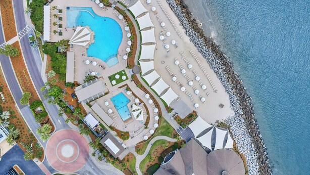 Oversigtsbillede af et resort med en stor swimmingpool, strand og flere parasoller.