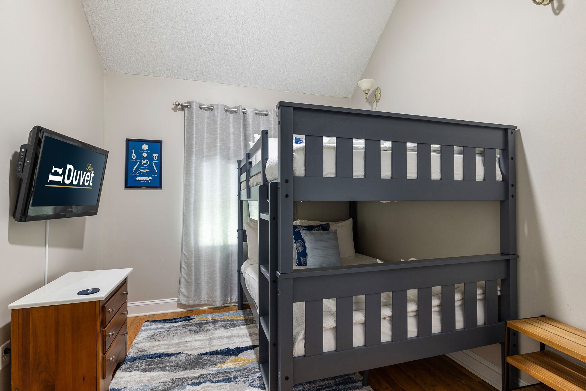 Ein Schlafzimmer mit Etagenbett, Fernseher, kleiner Holzschublade und gemustertem Teppich.