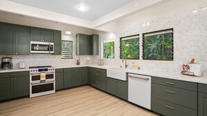 Une cuisine moderne avec des meubles de couleur verte, un plan de travail blanc, un four encastré et une fenêtre donnant sur un paysage verdoyant.