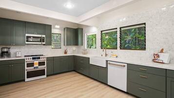 Een moderne keuken met groene kastjes, een wit aanrecht, een ingebouwde oven en een raam met uitzicht op groen.
