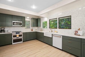 Eine moderne Küche mit grünen Schränken, einer weißen Arbeitsplatte, einem eingebauten Backofen und einem Fenster mit Blick auf Grünflächen.