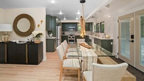 A modern kitchen with a central island, a dining area with a glass table, and a hanging light fixture.