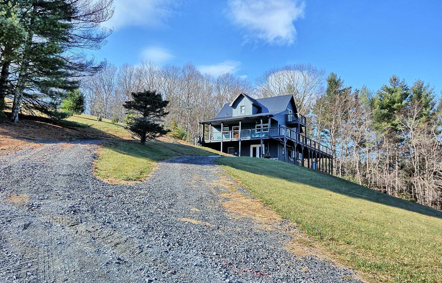 A two-story house with a balcony, surrounded by trees and a gravel path.