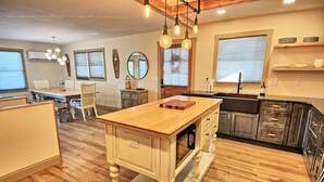 A kitchen with a central island, wooden flooring, pendant lighting, and a view of the living area. - Spacious 3BR chalet in Fleetwood, NC, perfect for family gatherings, sleeps 10. (Fleetwood)