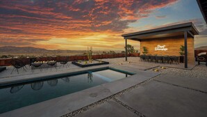 Zona de piscina con vistas al atardecer, mobiliario exterior y una estructura de madera con la inscripción 'Dreamscape'.