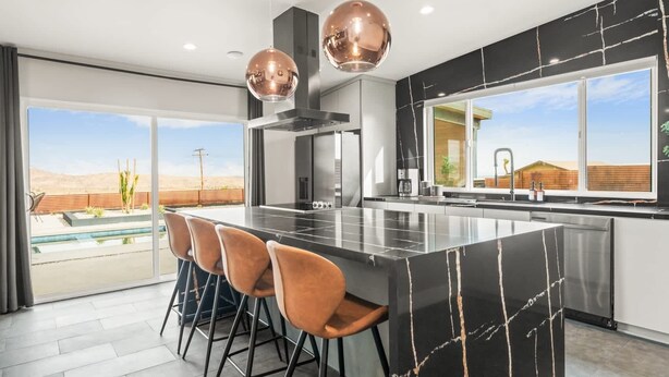 Una cocina moderna con una isla grande, taburetes de bar, luces colgantes y vistas a un paisaje desértico.