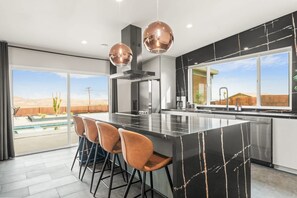 Une cuisine moderne dotée d’un grand îlot central, de tabourets de bar, de luminaires suspendus et offrant une vue sur un paysage désertique.