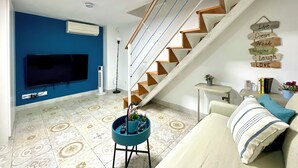 Una sala de estar con televisor, una escalera, una pared con letreros motivacionales y un sillón azul.
