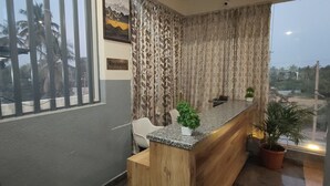 Un espace d’accueil comprenant un comptoir en bois, un bureau de réception et deux plantes en pot.