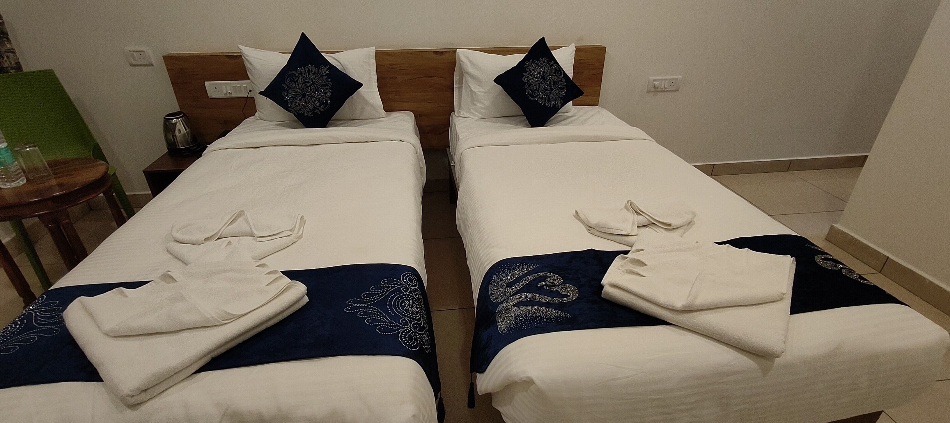 Zwei Einzelbetten mit weißen Laken und dunkelblauen Kopfteilen. Jedes Bett ist mit einem Zierkissen und einem gefalteten Handtuch ausgestattet.