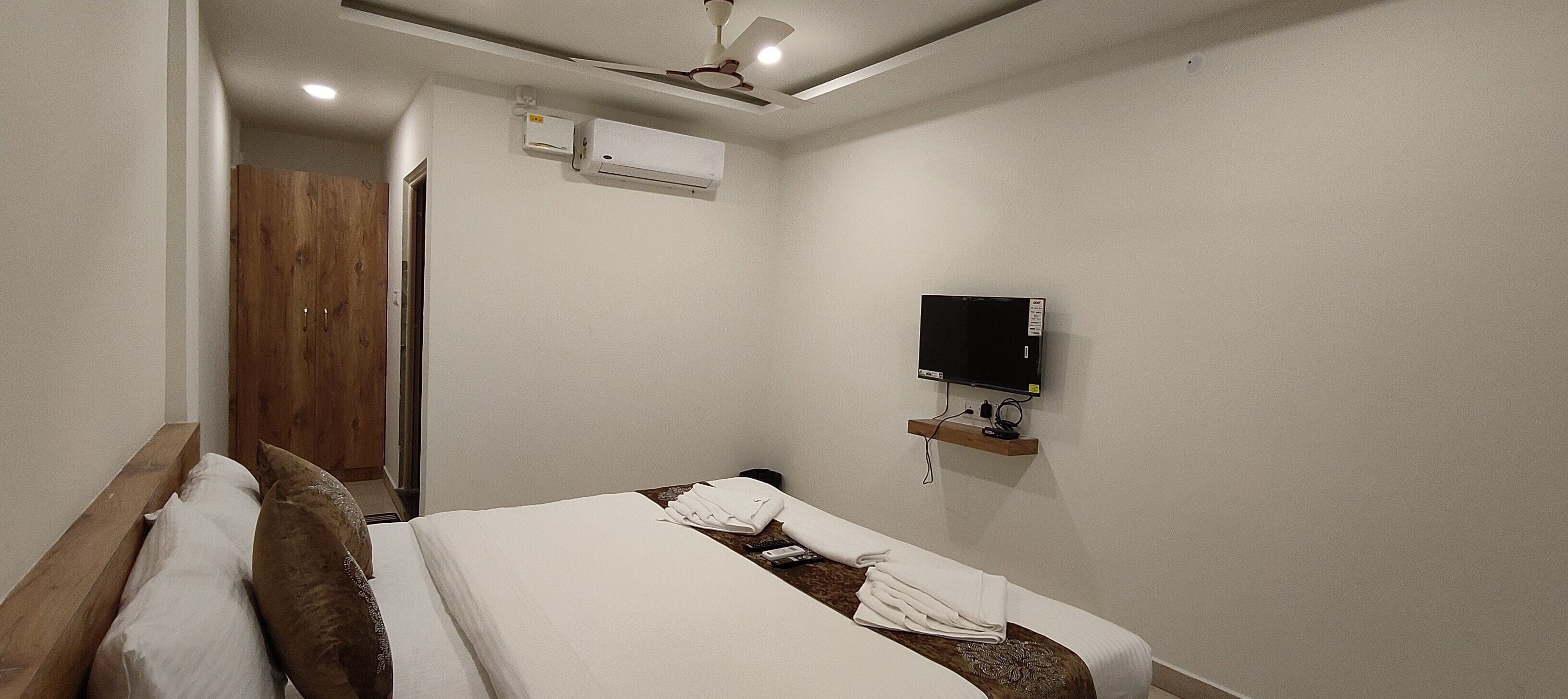 Habitación de hotel con cama, televisor montado en la pared, unidad de aire acondicionado y puerta de madera.