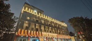 A multi-story hotel with illuminated wave patterns on the facade, large windows, and a ground-level restaurant. - Hotel Amulya Regency  (Devanahalli)