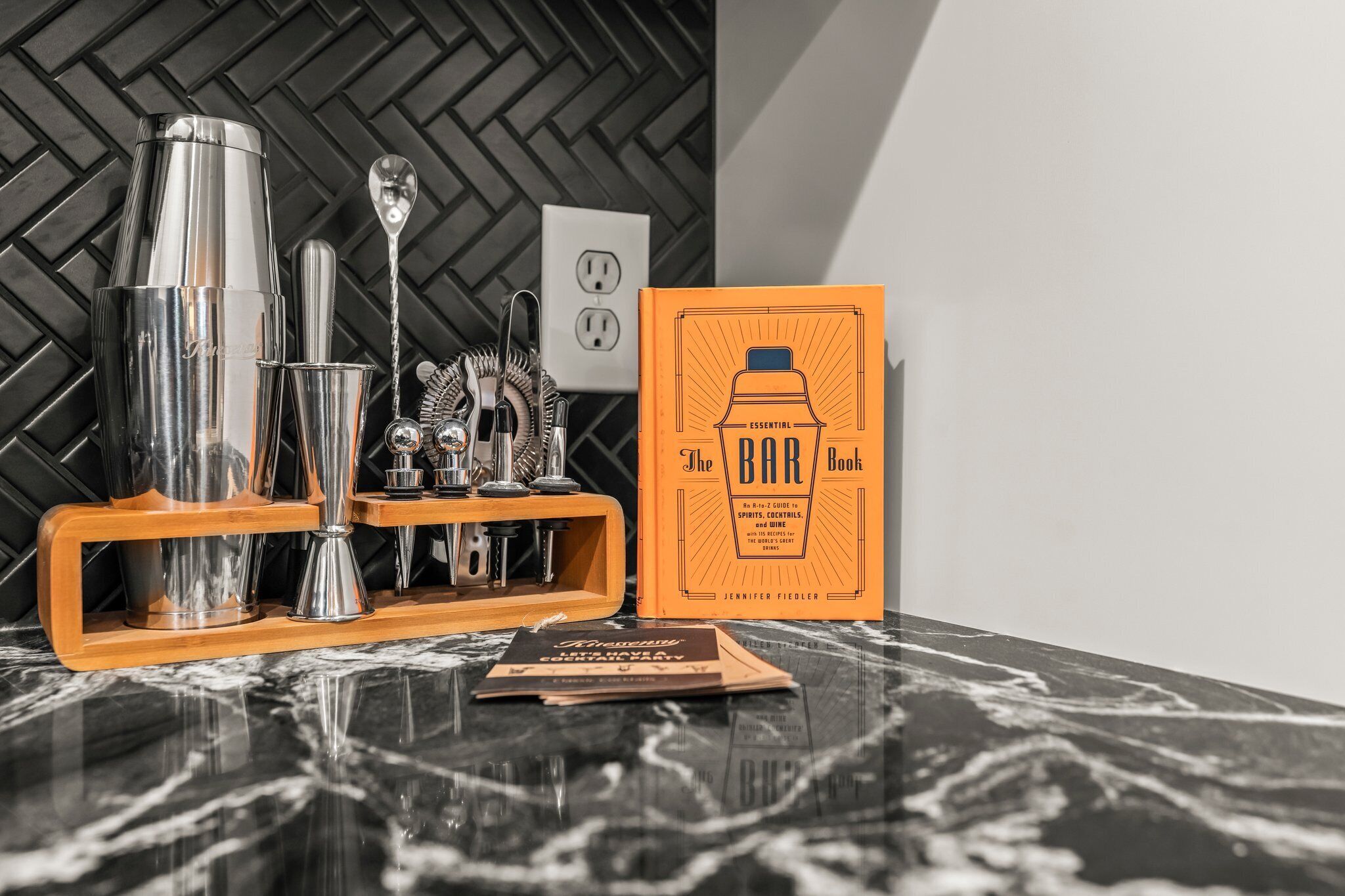 A bar setup with a cocktail shaker, jigger, and other bar tools on a marble countertop.