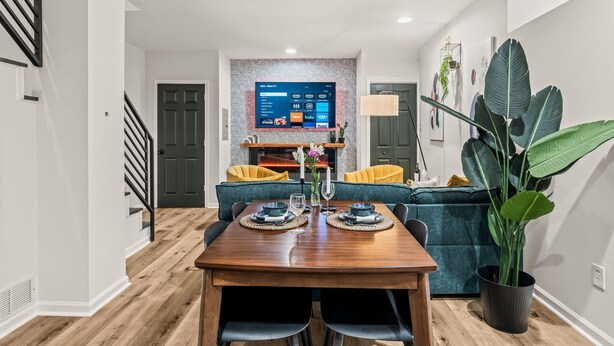 Un espace repas moderne avec une table en bois dressée pour deux personnes, un canapé et une grande plante en pot.