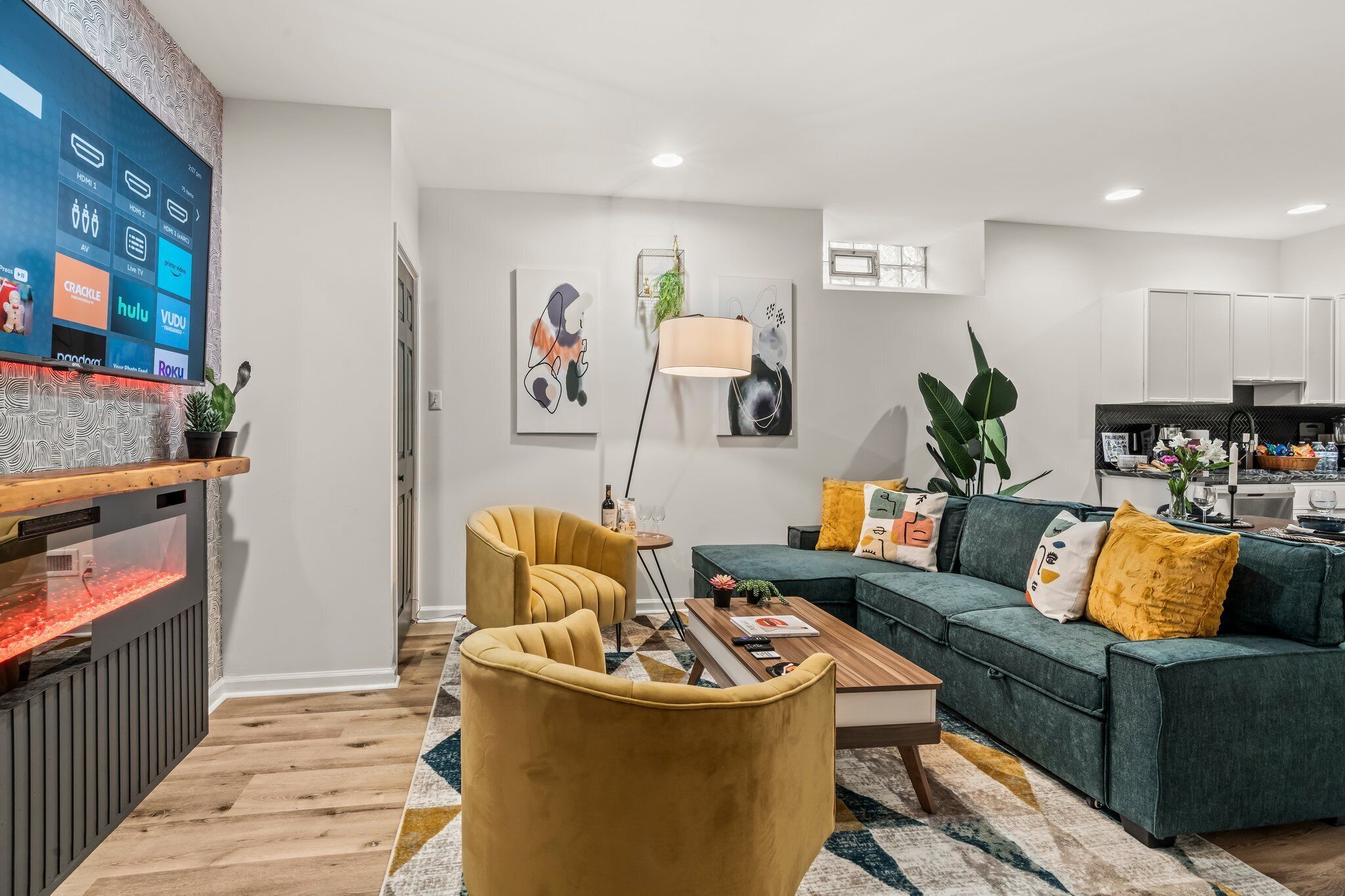 A modern living room with a green sofa, yellow armchairs, a coffee table, and a flat-screen TV displaying streaming services.
