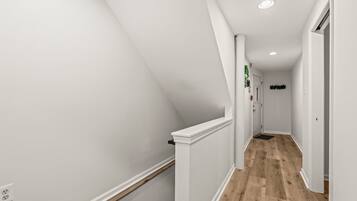 A narrow, white-walled hallway with a wooden floor and a white railing.