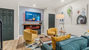 Un salon moderne avec un téléviseur à écran plat, deux fauteuils jaunes, un canapé bleu et une petite table d’appoint avec une lampe.