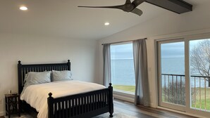 Een slaapkamer met een bed, nachtkastje en uitzicht op de zee door grote ramen.