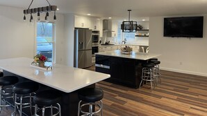 Een moderne keuken met een centraal eiland, barstoelen, roestvrijstalen apparatuur en een flatscreen televisie aan de muur.