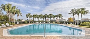 A rectangular swimming pool with a clear blue water surface, surrounded by palm trees and lounge chairs.