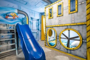 A children's play area with a blue slide, a ladder, and nautical-themed walls.