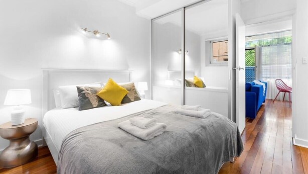 Moderni hotellihuone, jossa on suuri sänky, vaatekaappi ja oleskelualue, jossa on sininen sohva ja punainen nojatuoli.