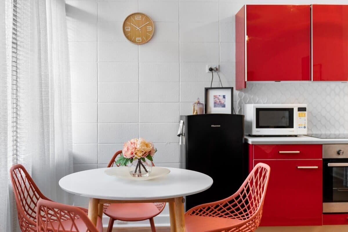 Een moderne keuken met rode kastjes, een zwarte koelkast, een witte magnetron en een ronde tafel met stoelen.