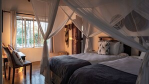 Une chambre avec deux lits, une fenêtre avec des rideaux, une chaise et un lit à baldaquin.