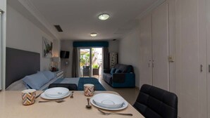 Una habitación de hotel moderna con una cama, una mesa de comedor dispuesta con platos y cubiertos, un sofá y vistas al exterior.